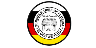 Seal of the Seminole Tribe of Florida with a chickee hut in the center, surrounded by black, white, red, and yellow bands, and the words IN GOD WE TRUST.