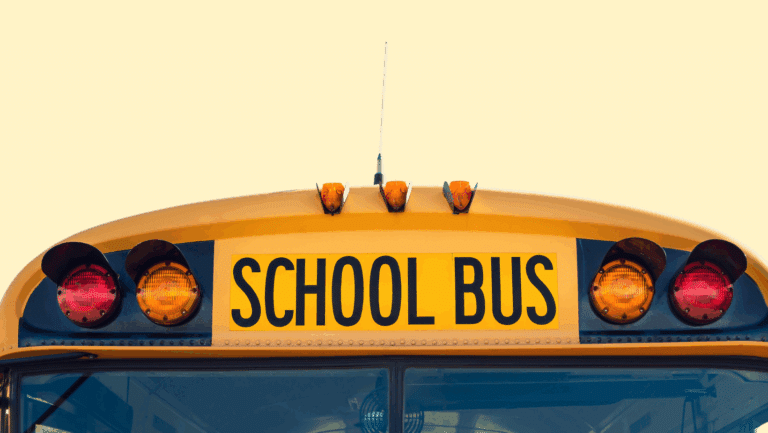 Close-up of the front top section of a yellow school bus from a school bus fleet, with the SCHOOL BUS sign and lights visible against a clear background.
